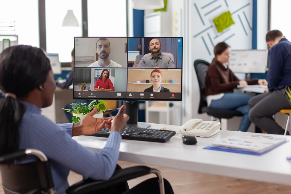 A hybrid work office featuring teammates on a video conferencing call and a worker at a desk.
